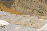 Pohled ze sedla do Francie, na skalách ohlazených ledovcem se sluní spousta turistů, kousek níž je chata Sarradets, která však odtud není vidět.